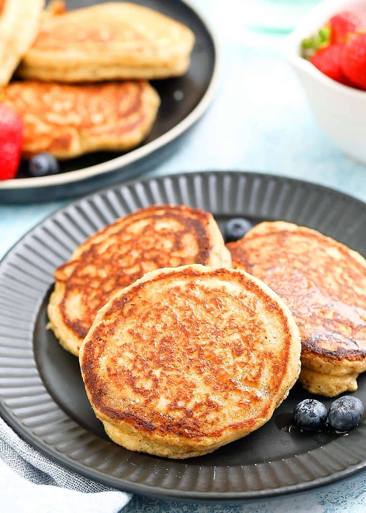 3 cooked pancakes placed on a black plate along with berries. 