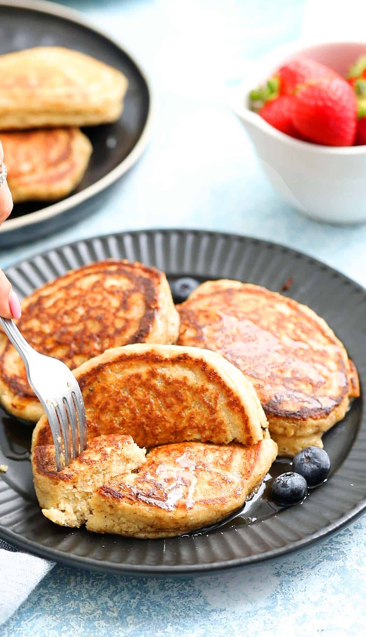 a hand removing a piece of cut pancake from a black plate.