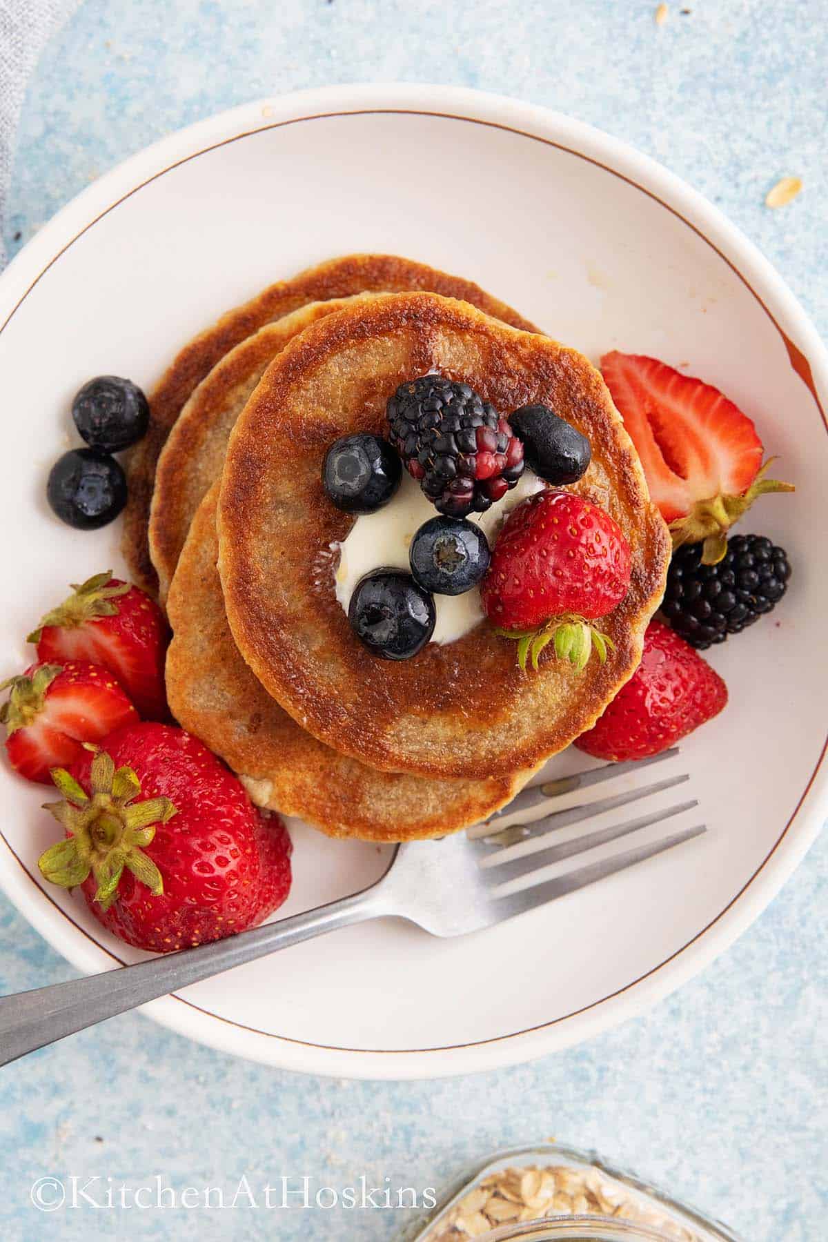 healthy pancakes in a white bowl topped with butter and berries.