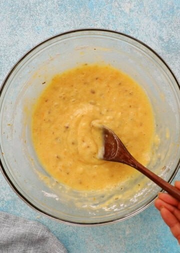 a hand mixing orange muffins batter in a glass bowl.