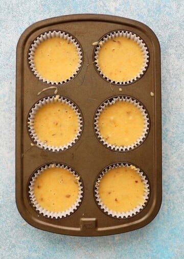 orange muffin batter filled in a 6 cup metal muffin pan.