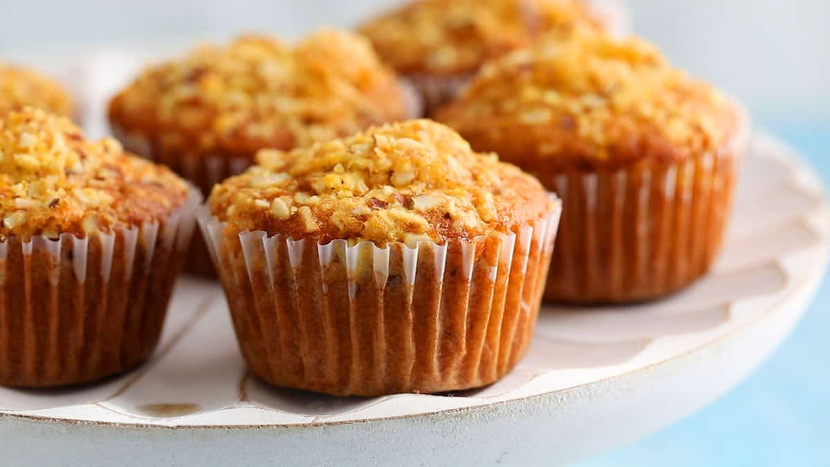 6 baked orange muffins placed in a white cake stand.