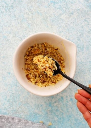 a hand mixing chopped almonds and sugar in a small white bowl using a black spoon.