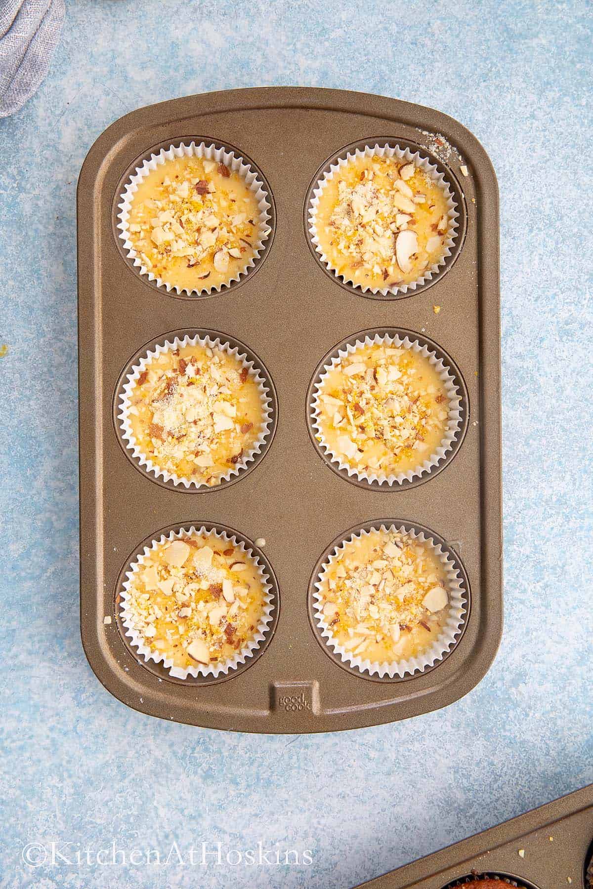 cup cake pan with orange batter and topped with almonds. 