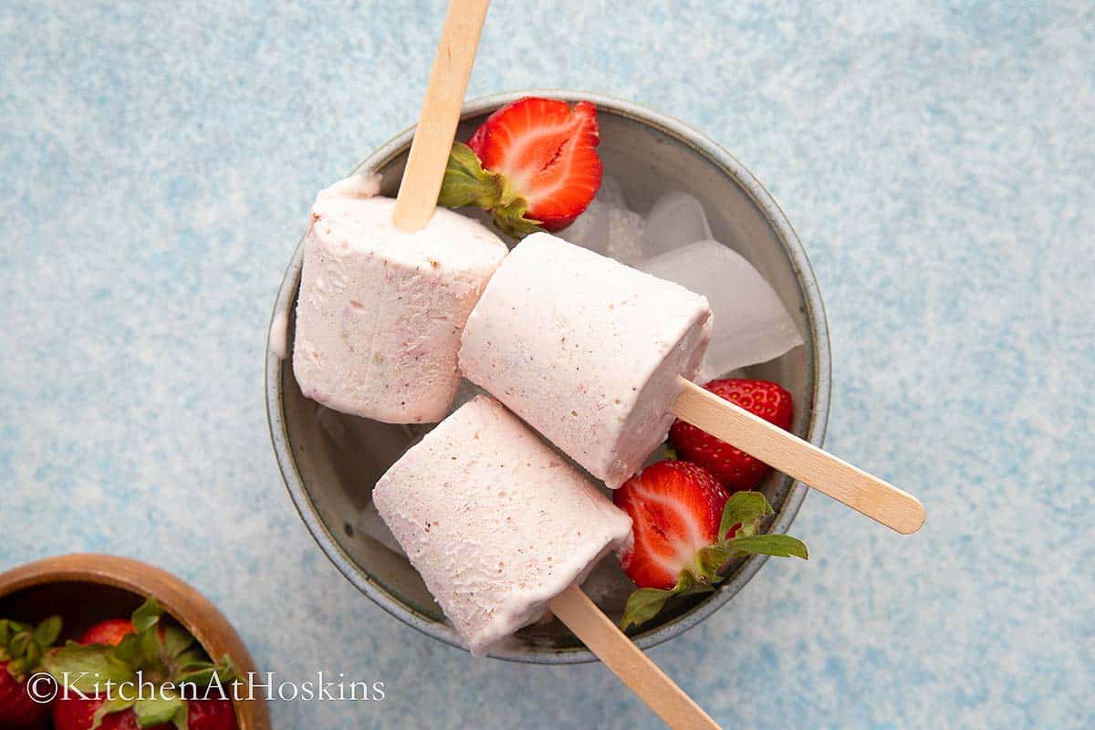 kulfi on a bowl filled with ice along with cut strawberries.