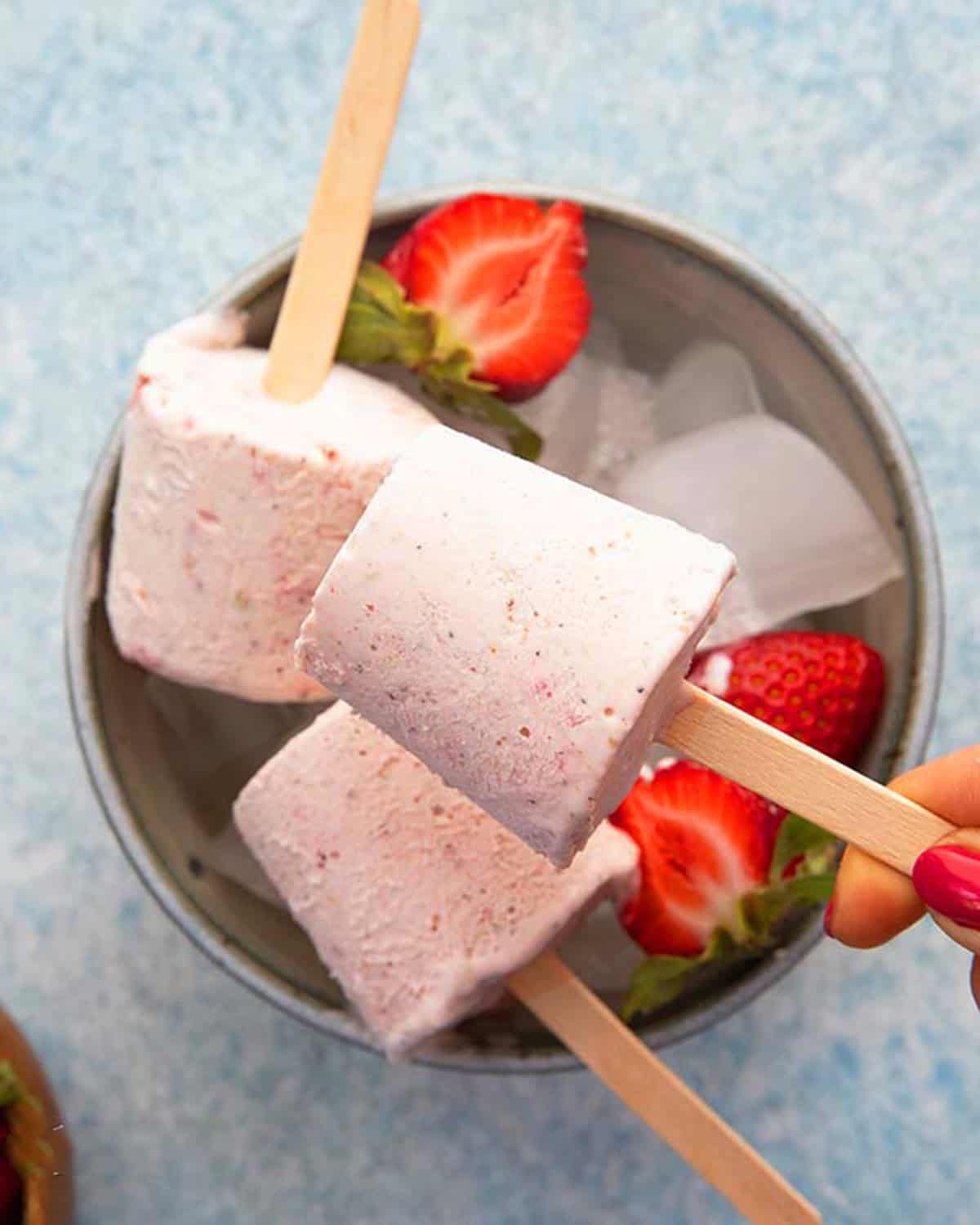 3 strawberry kulfi ice cream popsicles in a blue bowl.