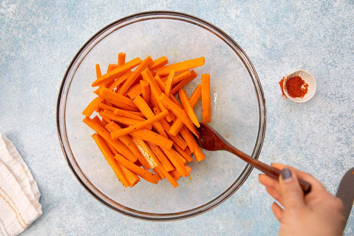 tossing carrot sticks with oil and seasonings in a glass bowl.