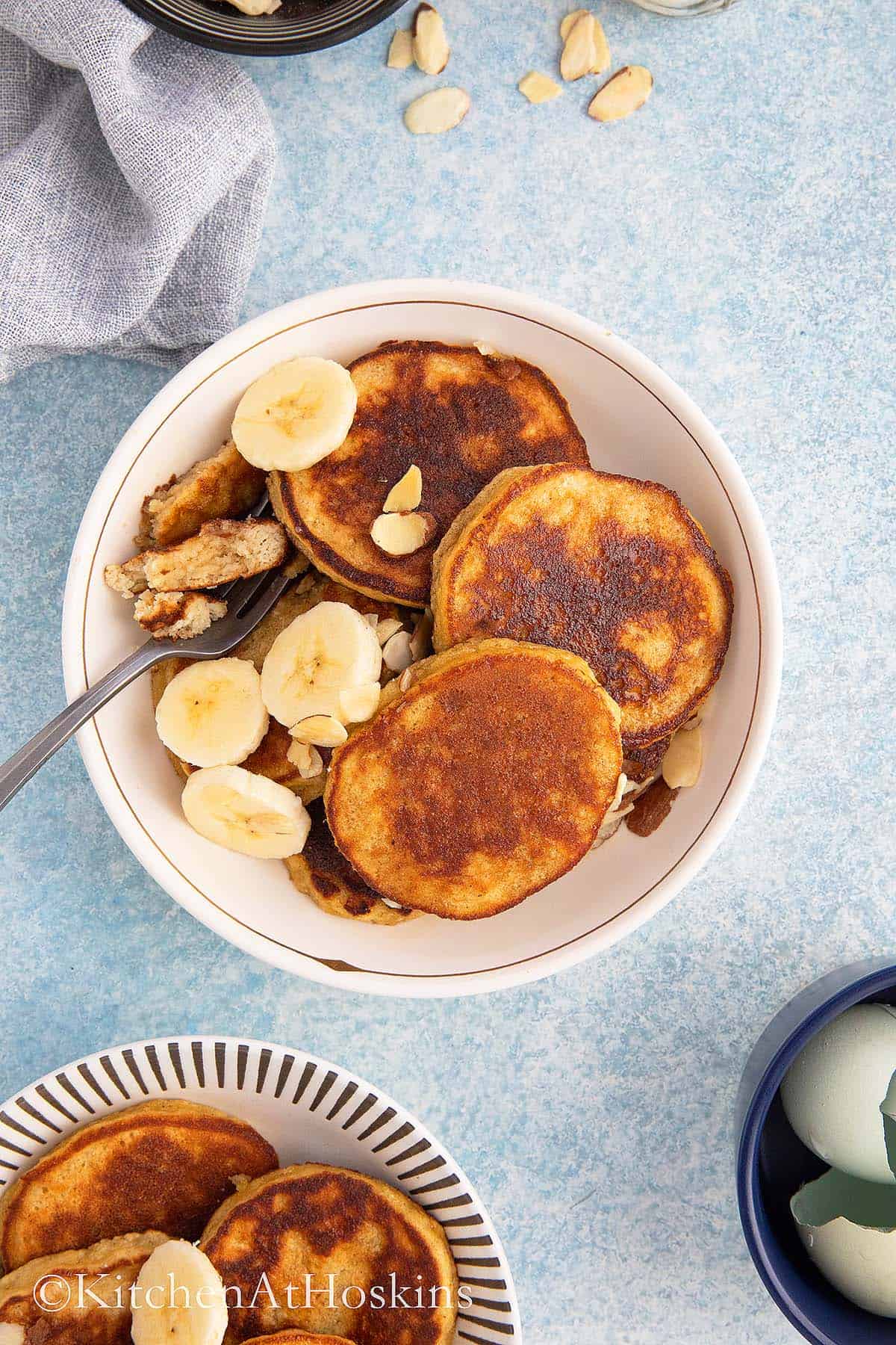 ALMOND FLOUR PANCAKES IN A BOWL TOPPED WITH SLICED BANANAS AND ALMONDS.