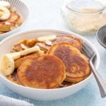 3 banana pancakes topped with sliced bananas in a white bowl.
