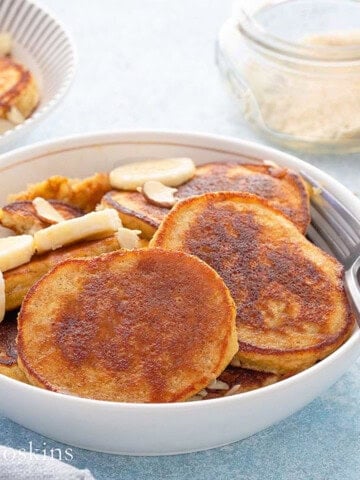 3 banana pancakes topped with sliced bananas in a white bowl.