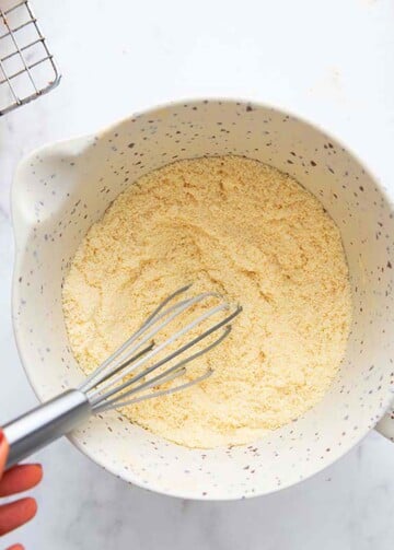 a hand whisking white flour in a white bowl.