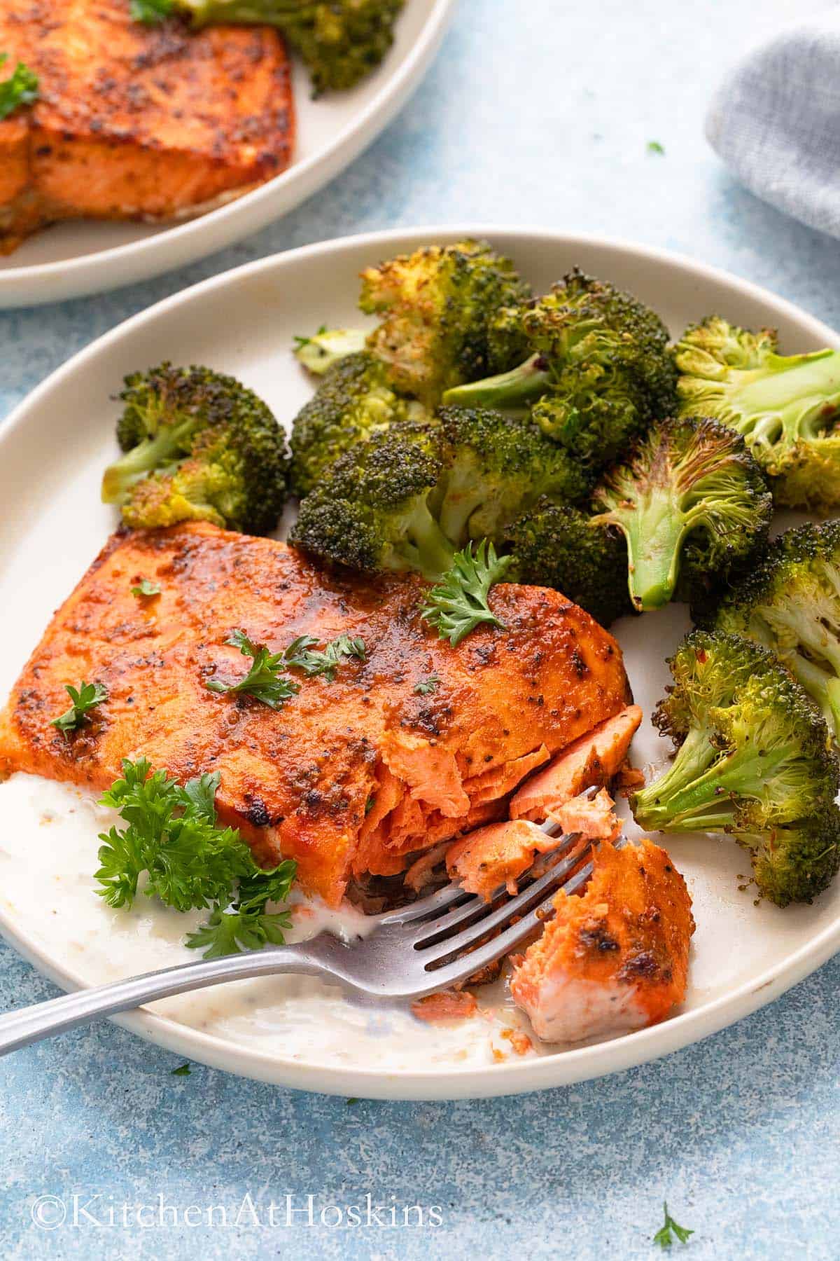 cooked spicy salmon fillet on a white plate with roasted broccoli.