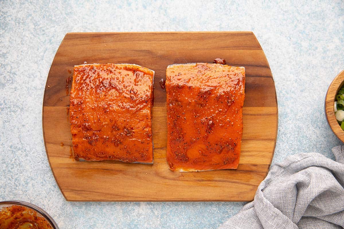 marinated salmon fillets on a wooden cutting board.