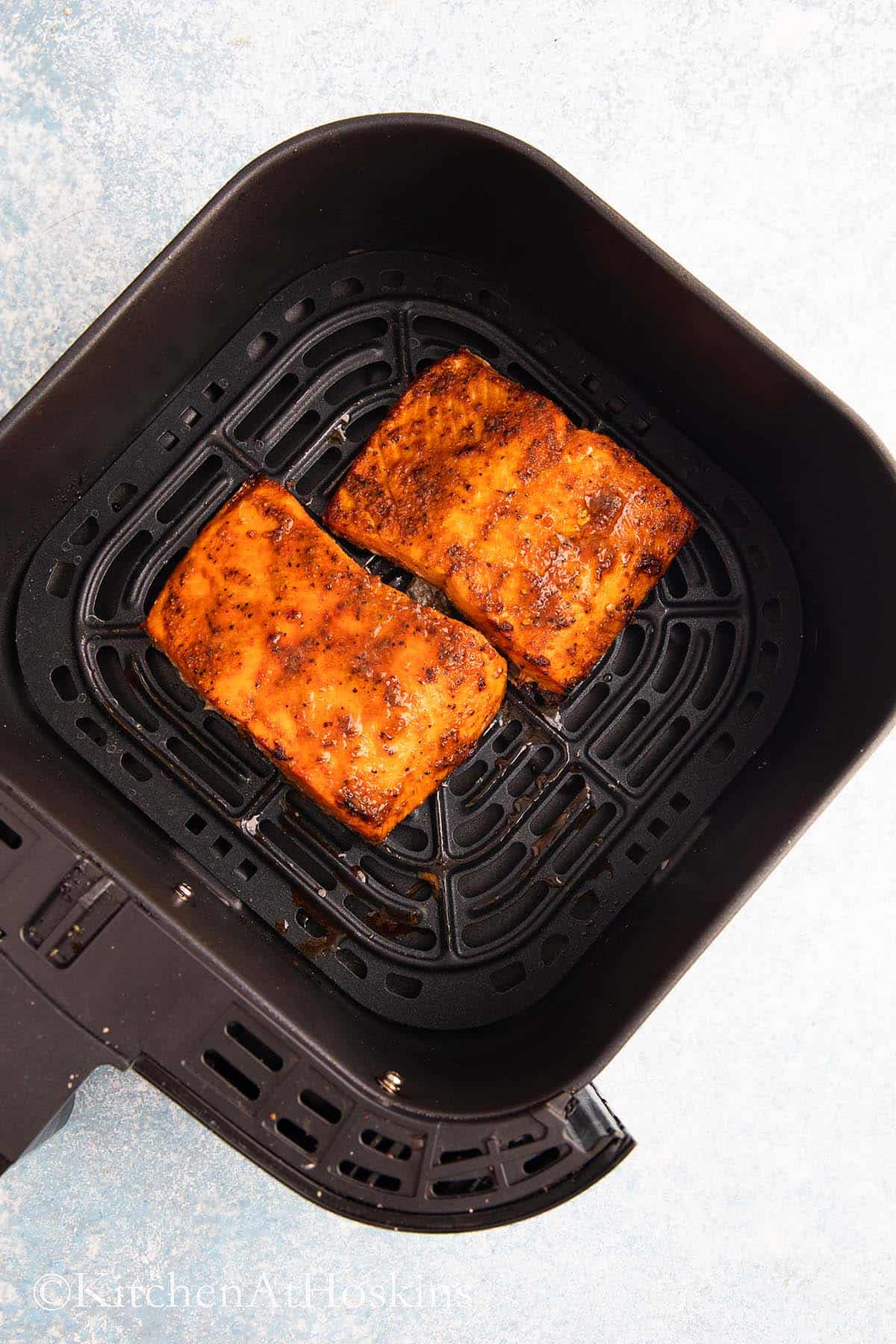 cooked spicy salmon fillets in an air fryer basket.