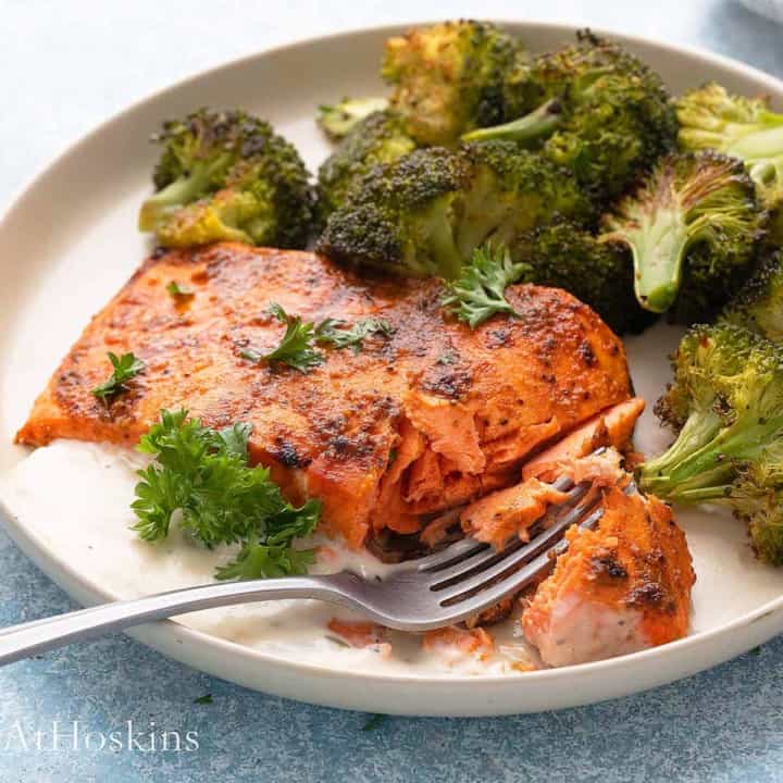 air fried salmon on a white plate with broccoli along with a fork.