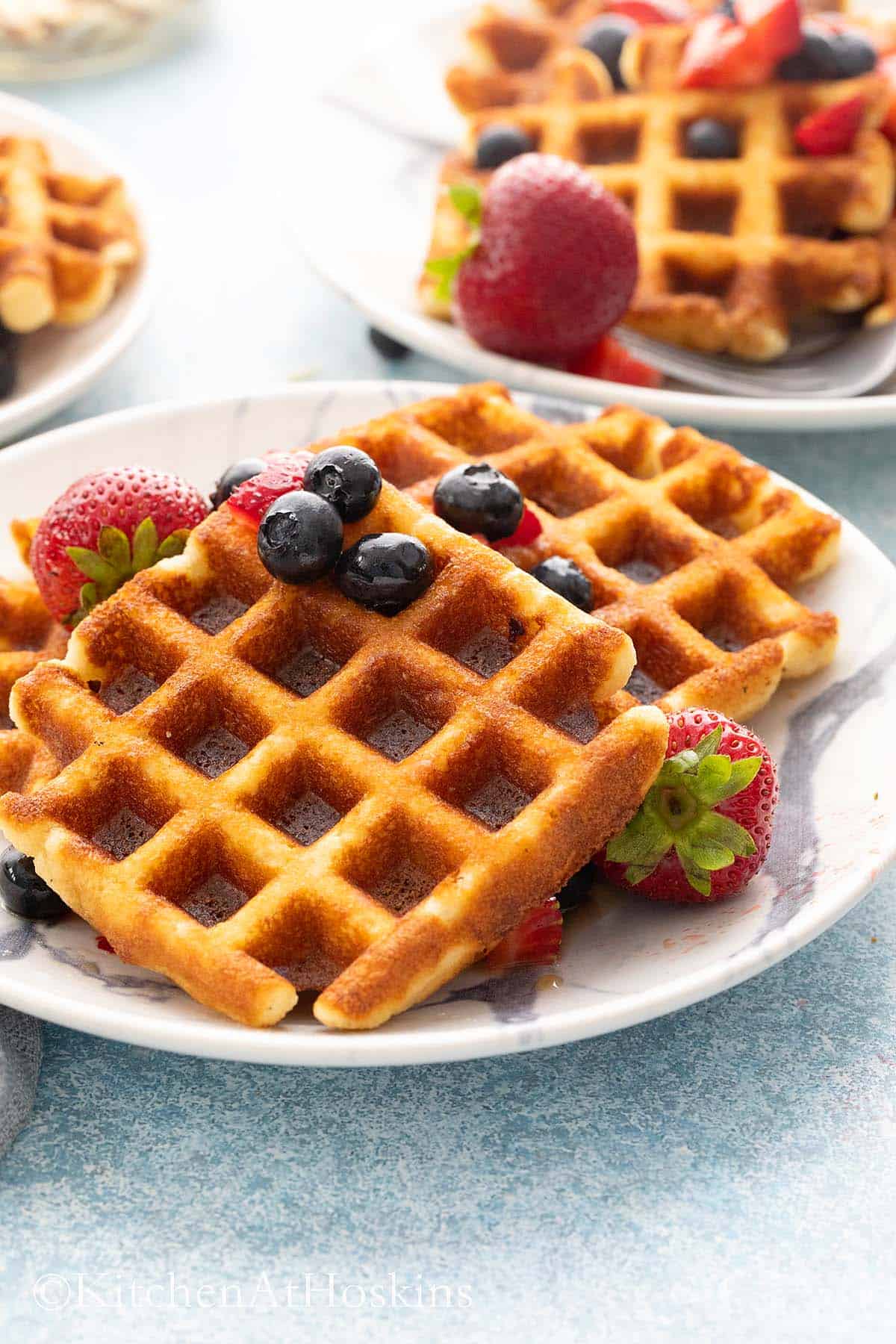 white plates with gluten free Belgian waffles, topped with strawberry.
