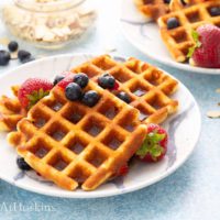 white plate with crisp almond flour waffles topped with berries.