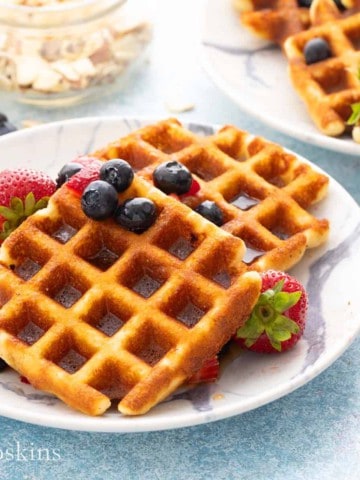 white plate with crisp almond flour waffles topped with berries.