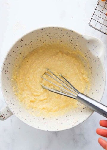 a hand whisking almond flour waffle batter in a white bowl.