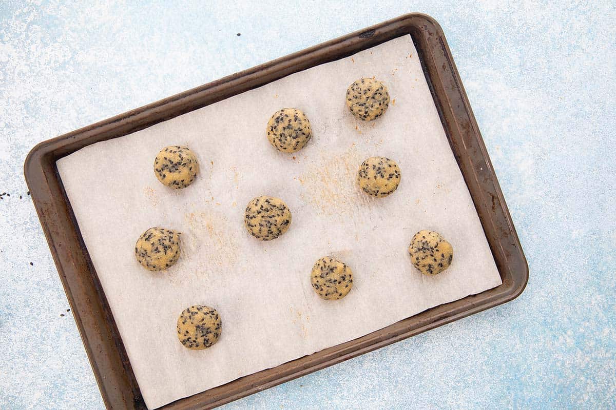 shaped sesame seed cookie dough on a parchment lined baking sheet.