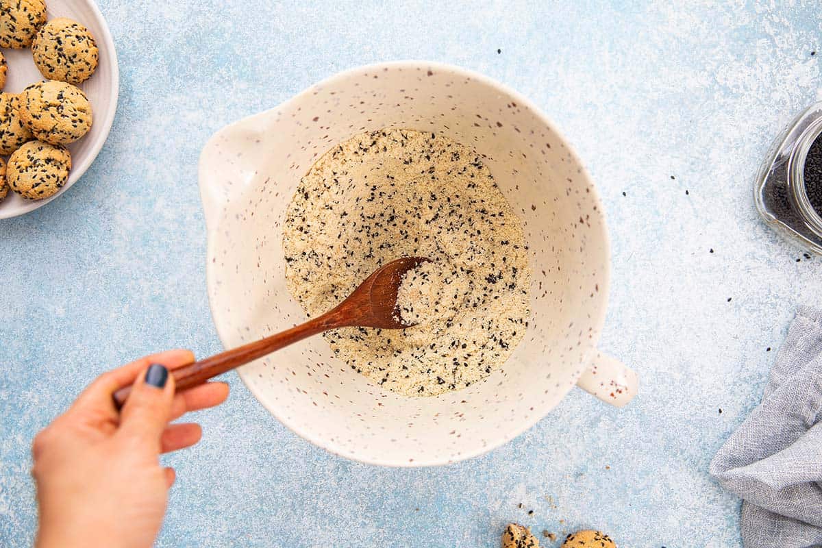 a hand mixing dry ingredients in a bowl with a wooden spoon.