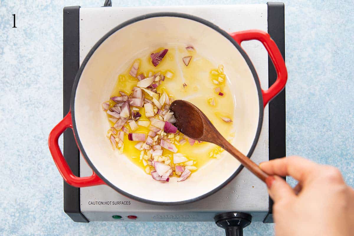 a hand sauteing chopped onion and garlic in some oil.