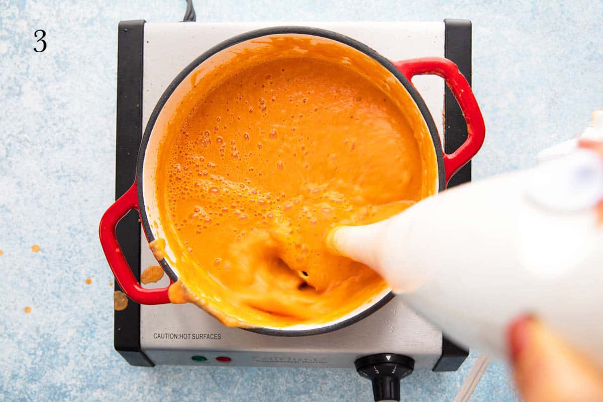 a hand blending chickpea soup using a white immersion blender.