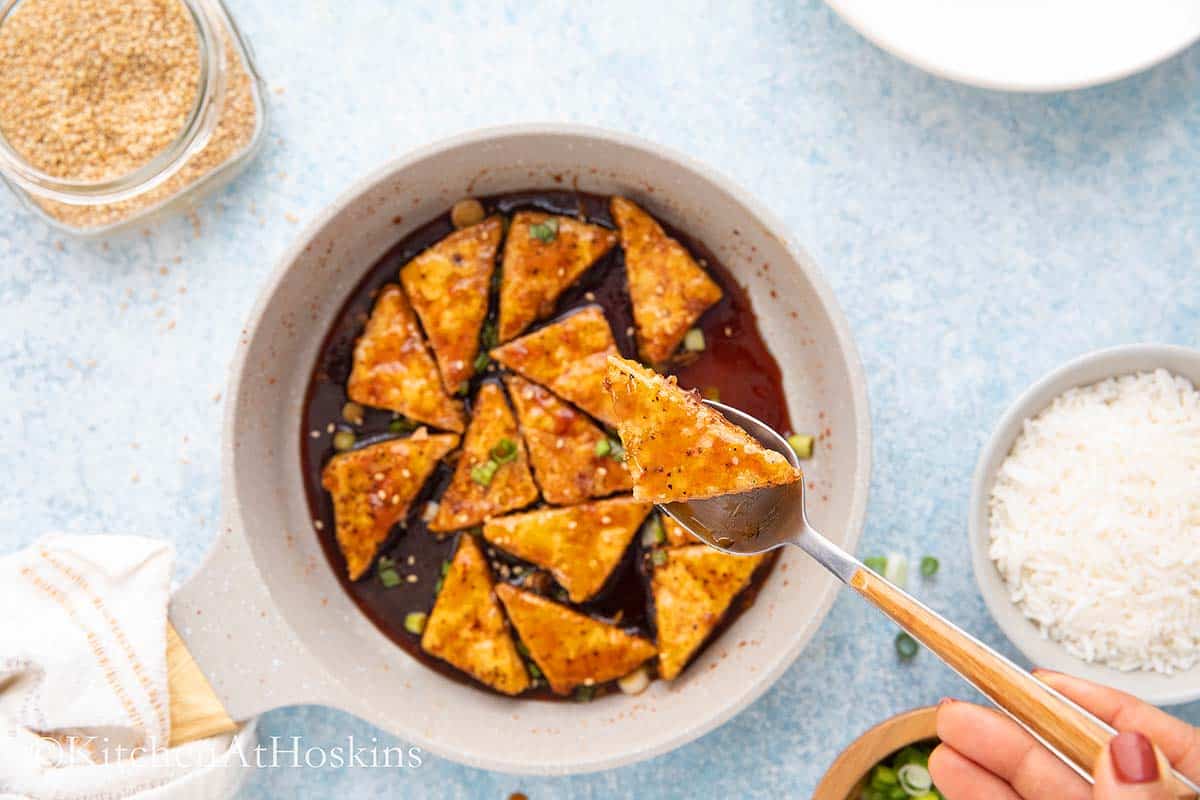 a spoon lifting a fried tofu from a pan.