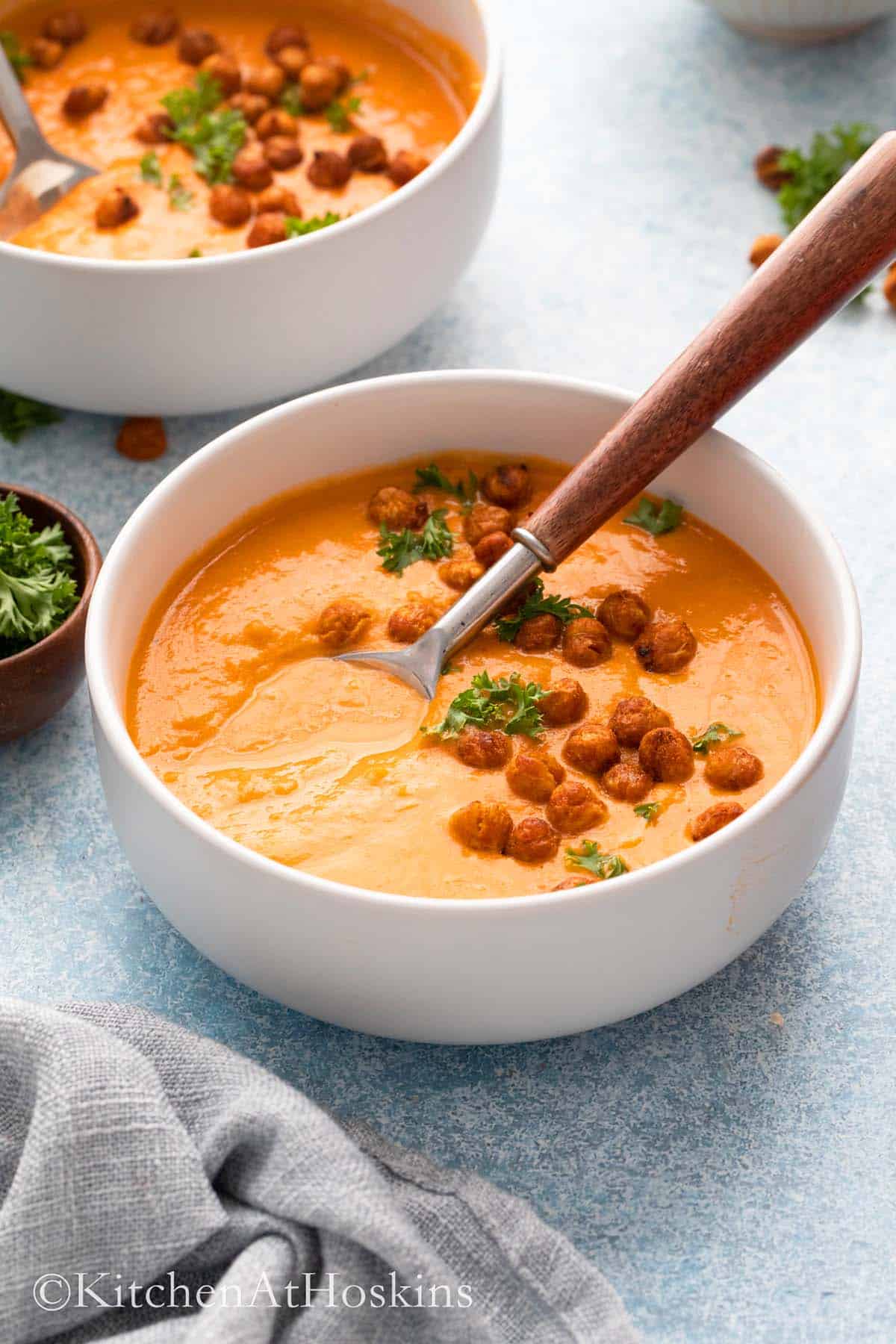 2 white bowls with chickpea soup topped with parsley and crispy beans.