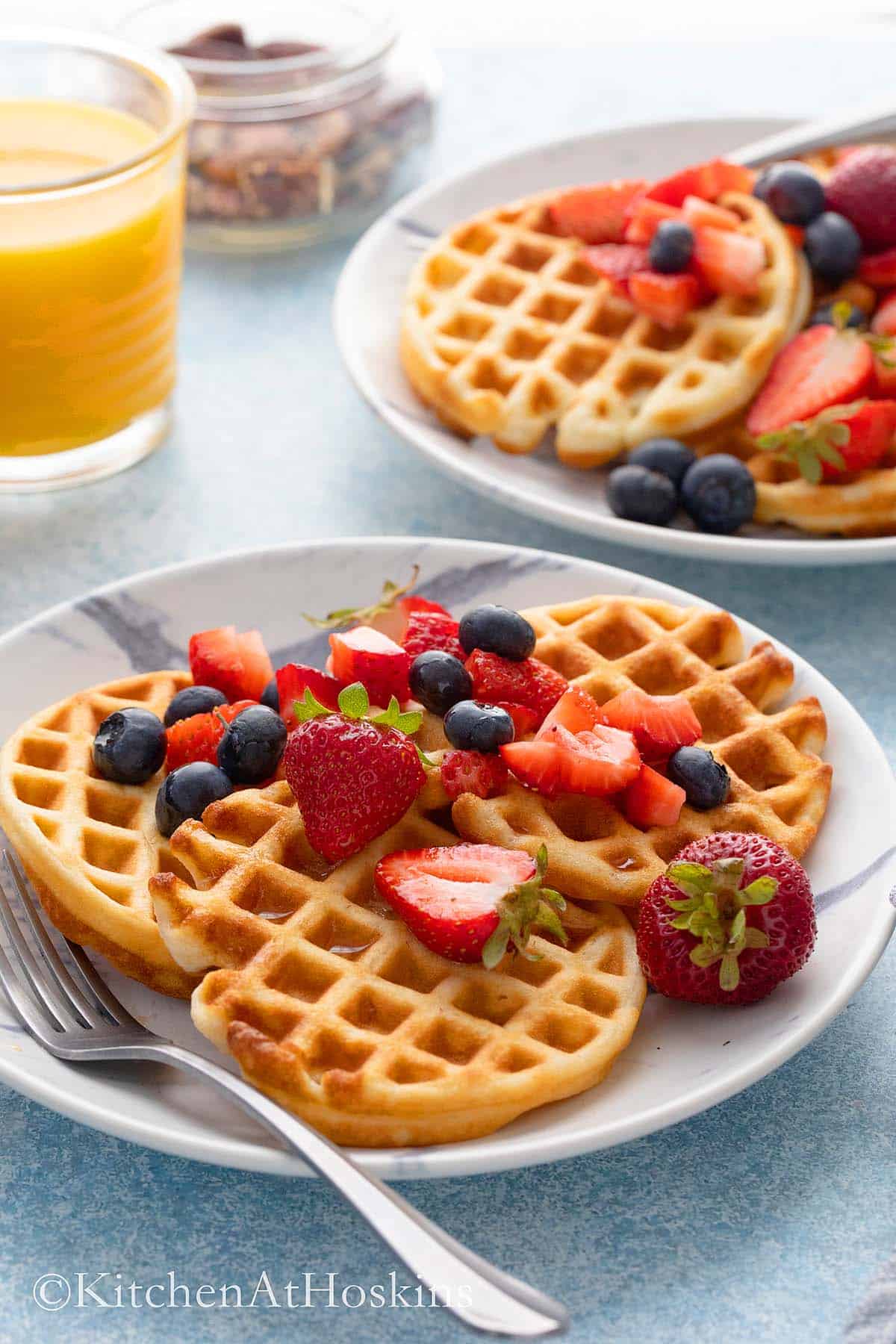 2 white plates with small waffles along with orange juice.