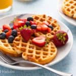 mini waffles on a white plate topped with berries and syrup.