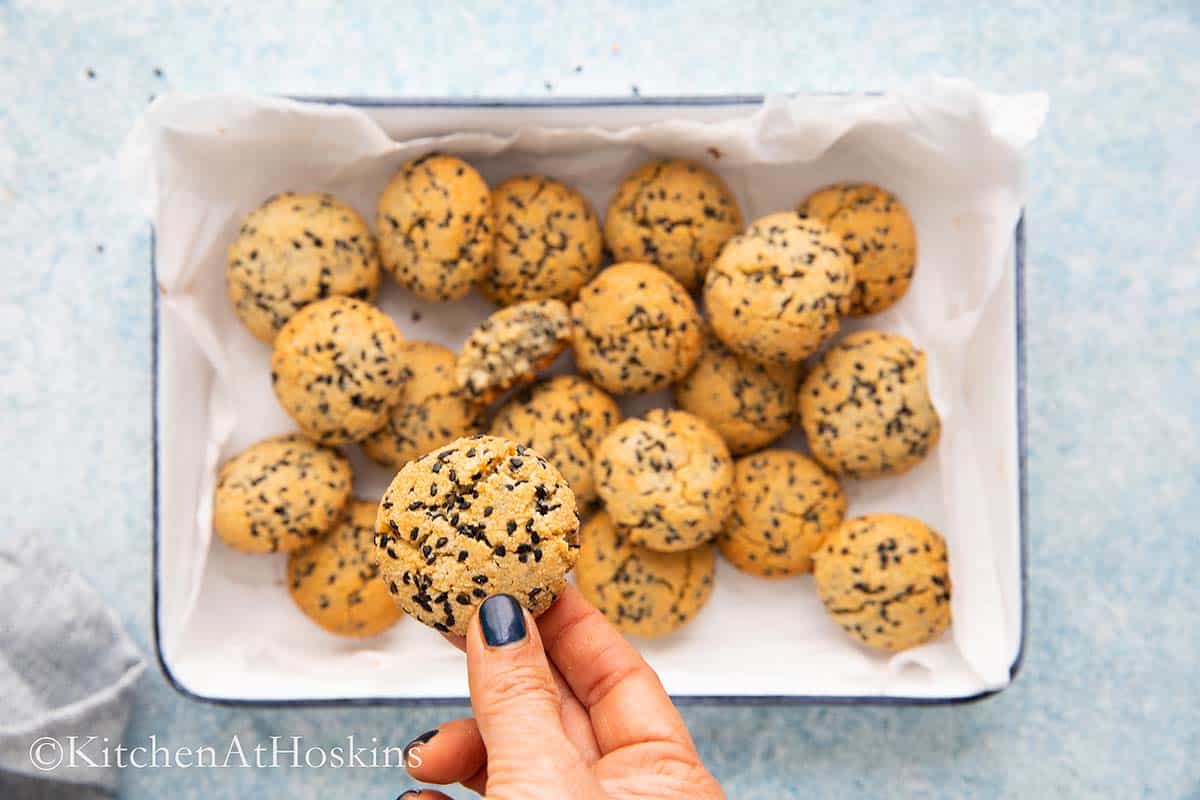 a hand holding a baked cookie above a tray filled with the same.