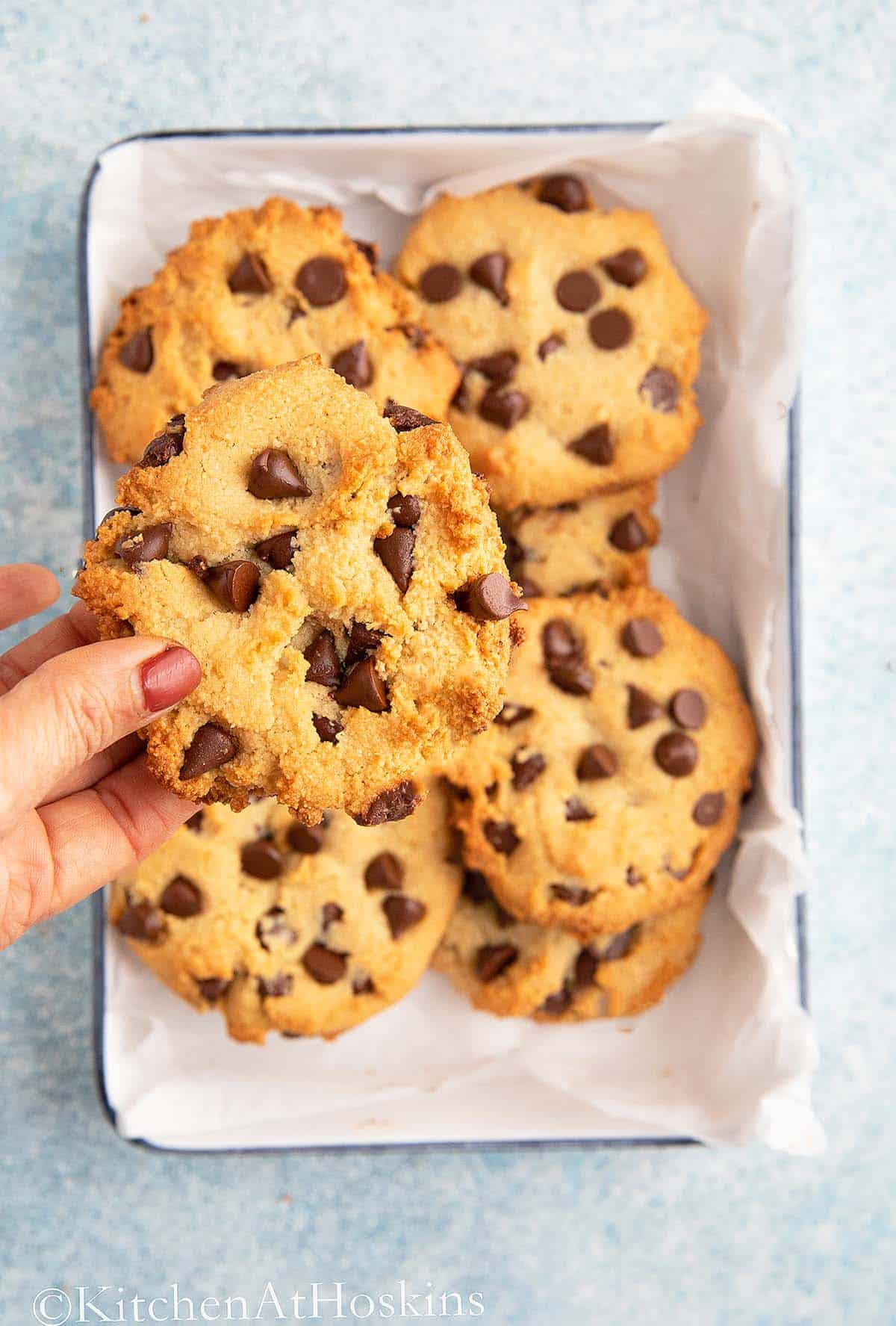 hand holding one cookie on top of a tray filled with more cookies.