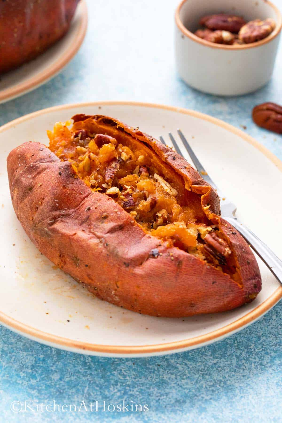 cooked sweet potato on a plate split open and filled with pecans and sugar.