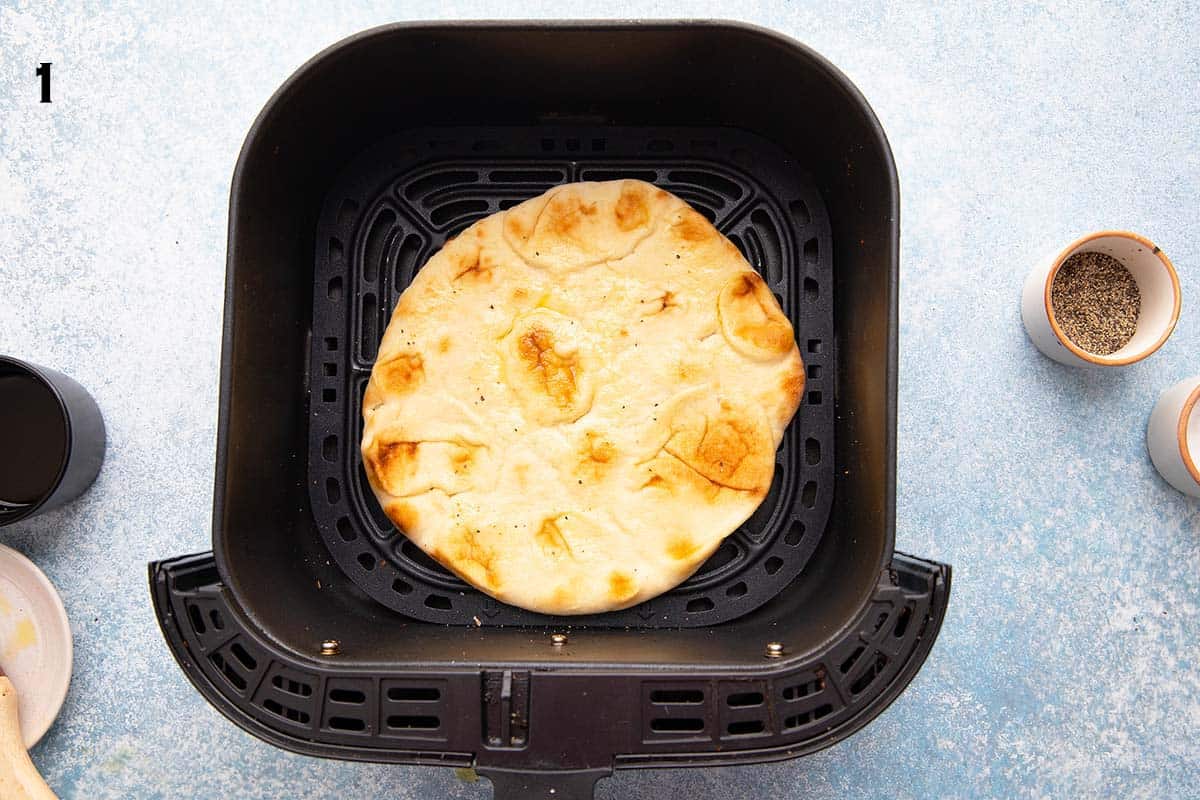a naan bread placed in an air fryer basket.