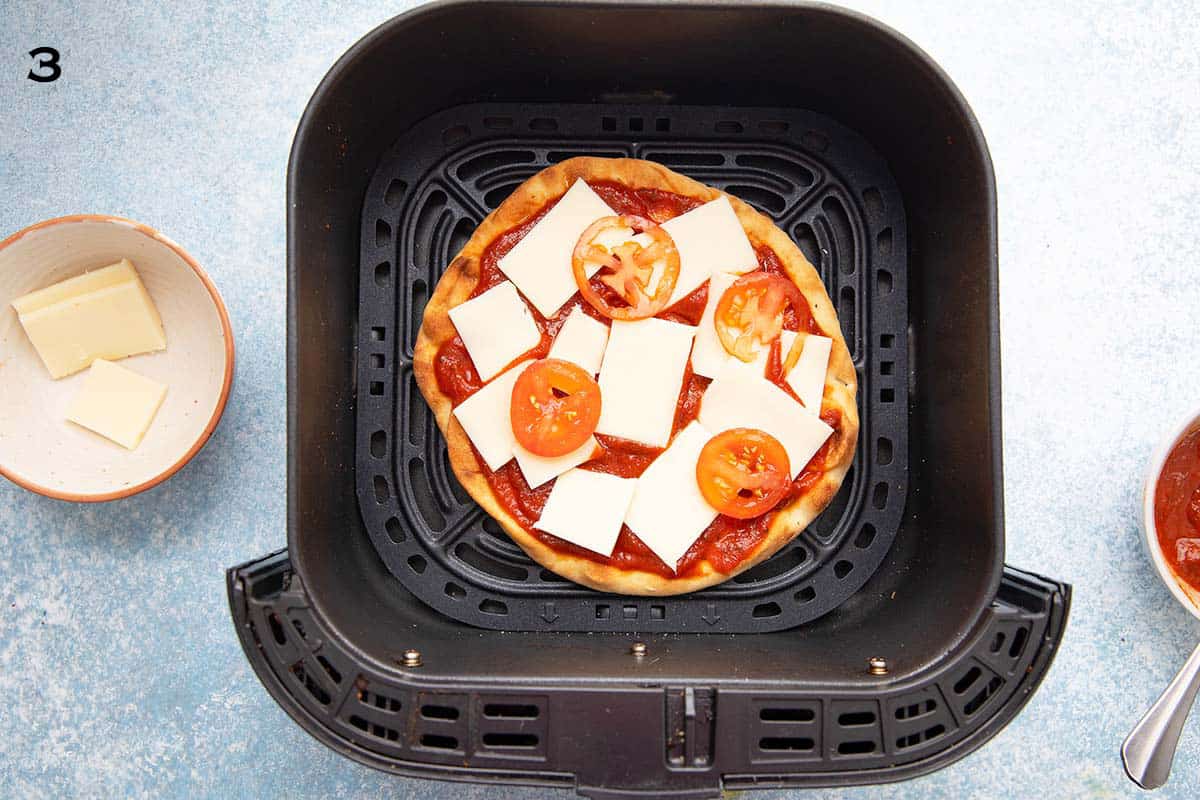 air fryer basket with a naan topped with pizza toppings.