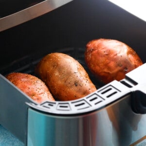 3 cooked sweet potatoes in an air fryer basket.