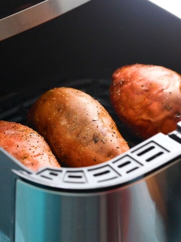 3 cooked sweet potatoes in an air fryer basket.