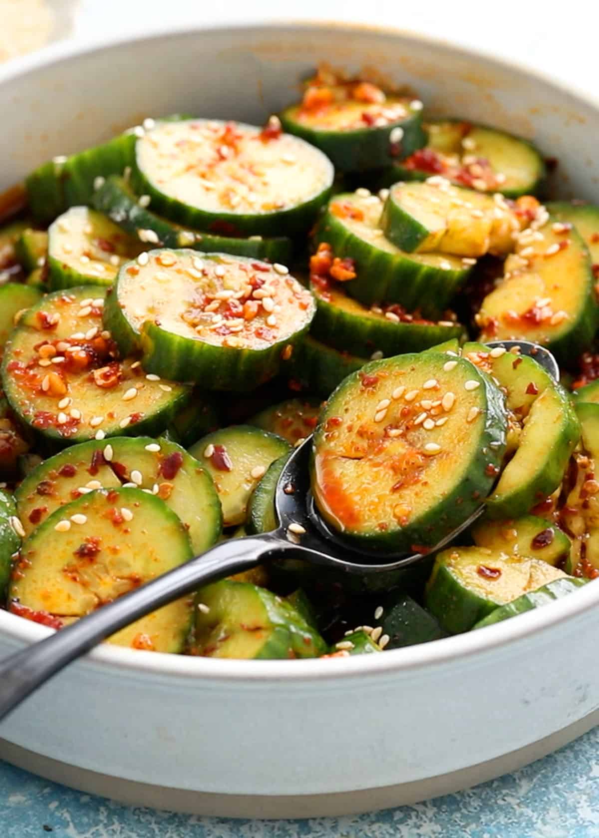 spiced sliced cucumbers in a round white bowl along with a spoon.
