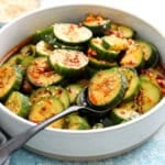 spiced sliced cucumbers in a round white bowl along with a spoon.