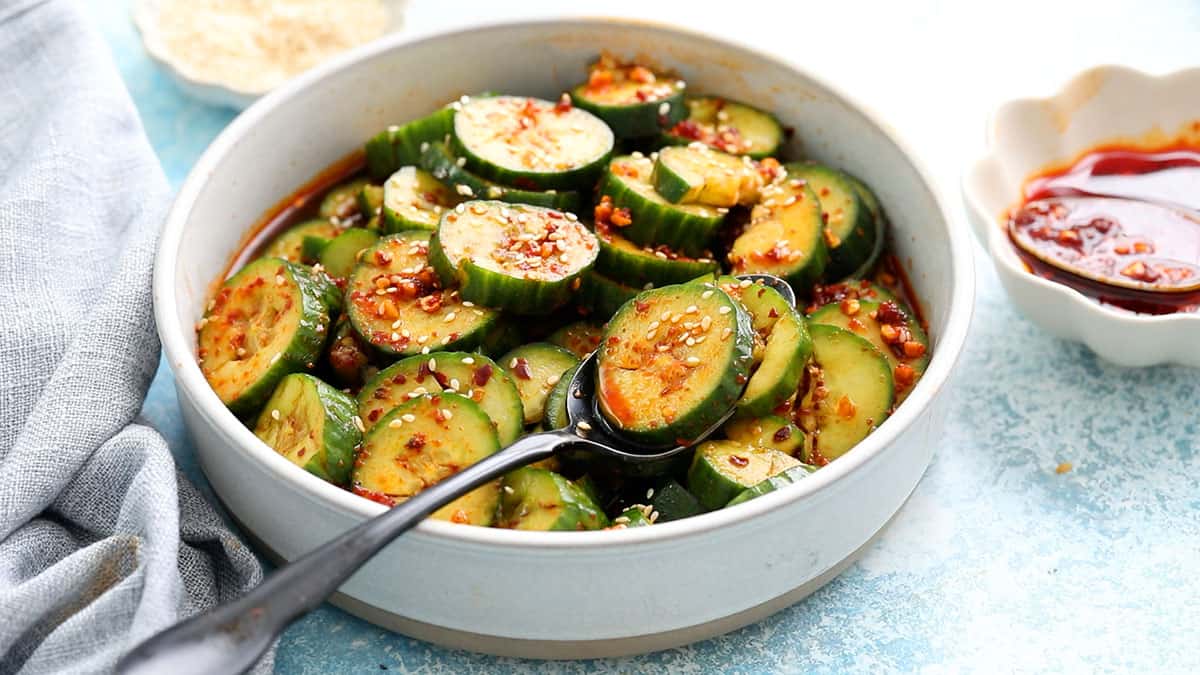 spiced sliced cucumbers in a round white bowl along with a spoon.
