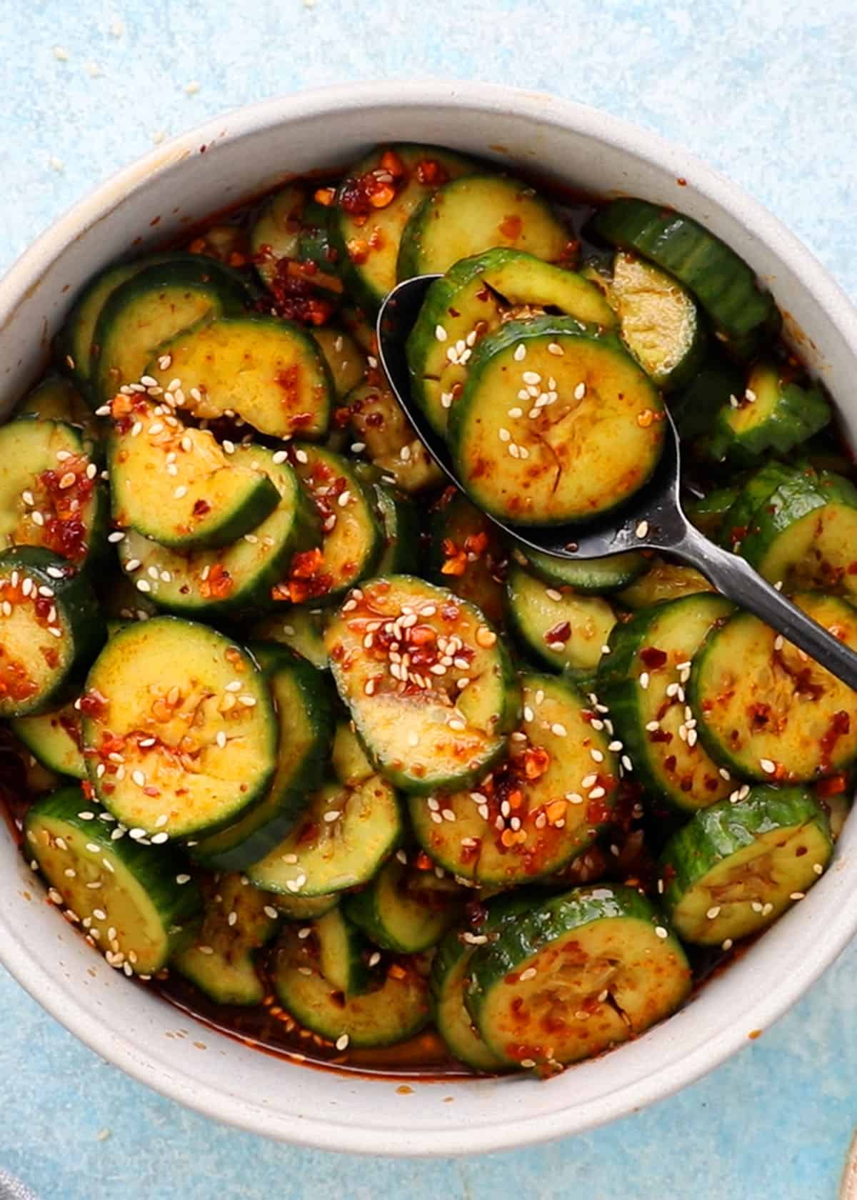 spiced sliced cucumbers in a round white bowl along with a spoon.