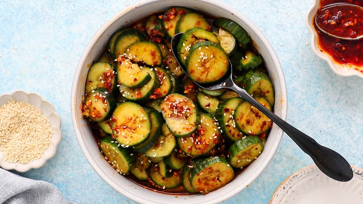 spiced sliced cucumbers in a round white bowl along with a spoon.