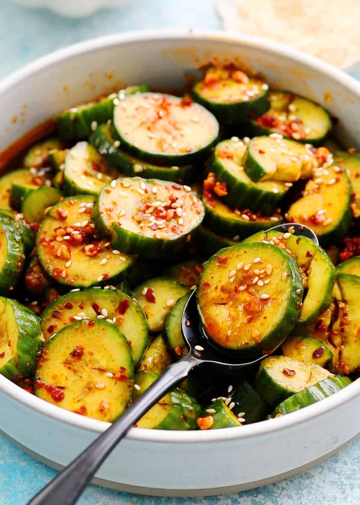 spiced sliced cucumbers in a round white bowl along with a spoon.