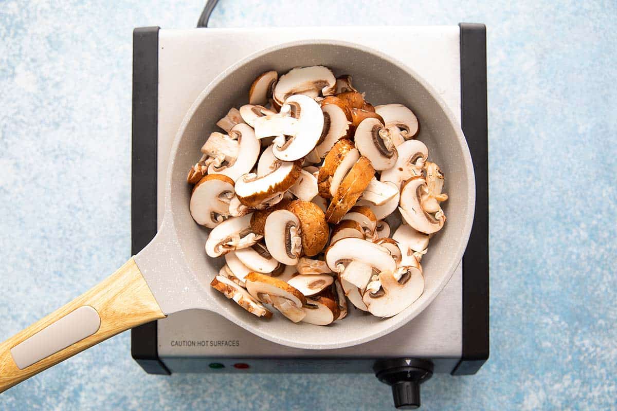sliced baby bella mushrooms in a skillet cooking on a stove.