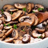 sauteed mushrooms in a skillet with a wooden spoon.