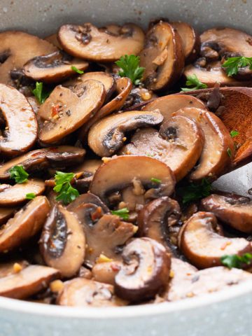 sauteed mushrooms in a skillet with a wooden spoon.