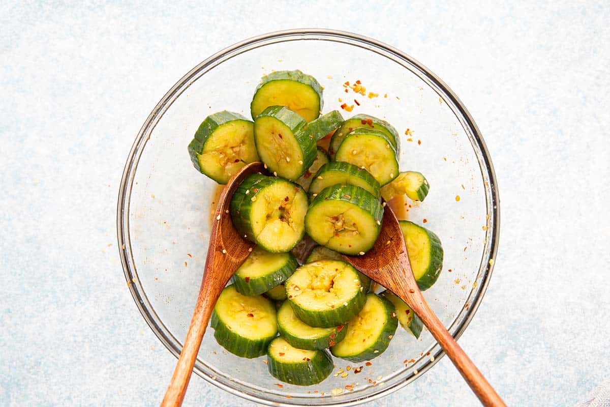 tossing sliced cucumber with spicy dressing in a bowl.
