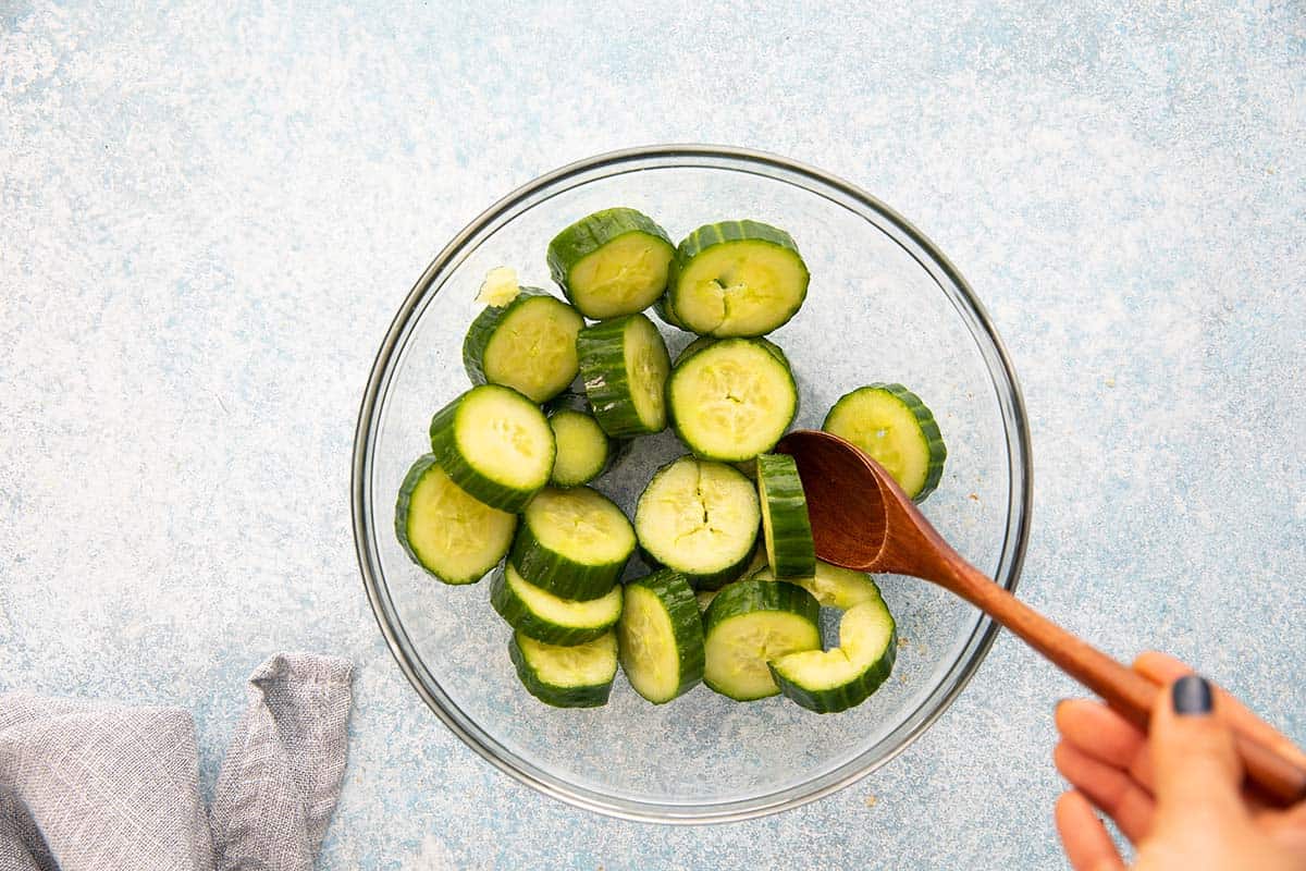 stirring sliced cucumber with salt in a glass bowl.