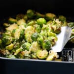 a flat spatula lifting cooked brussels sprouts from an air fryer baset.